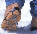 The bottom of a work-boot worn by a person walking on snow, showing what the device looks like when attached.