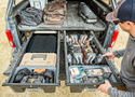 Back end of silver pickup truck showing raised bed with luggage on it & 2 full-length drawers slid out to show tools in them.