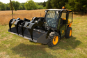 Yellow & black skid loader in field with black add-on grapple with 4 grapples o
ver top of loader bucket.