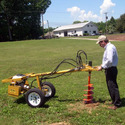 Wheeled post-hole digger with a man at the controls digging a hole in a field