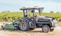 Monarch Electric Autonomous Tractor in a field towing a John Deere bush hog mower